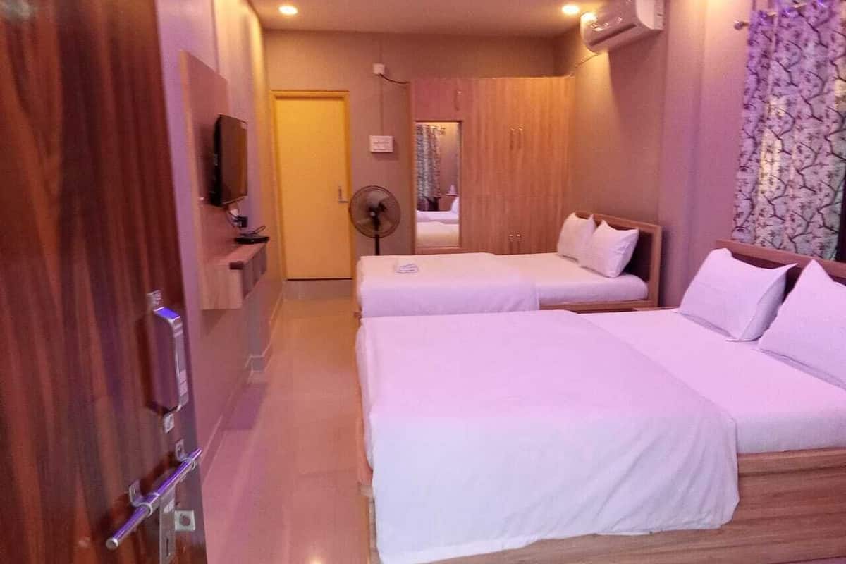 A hotel room with two beds, a wooden wardrobe, a TV, and a fan.