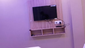 A television mounted on a wall with a wooden shelf below it. - 3 Star Lodge (North Lakhimpur)