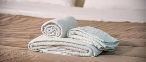 A bed with a patterned bedspread and rolled white towels.