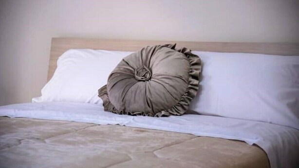 Una cama con cabecera de madera, ropa de cama blanca y una almohada decorativa.