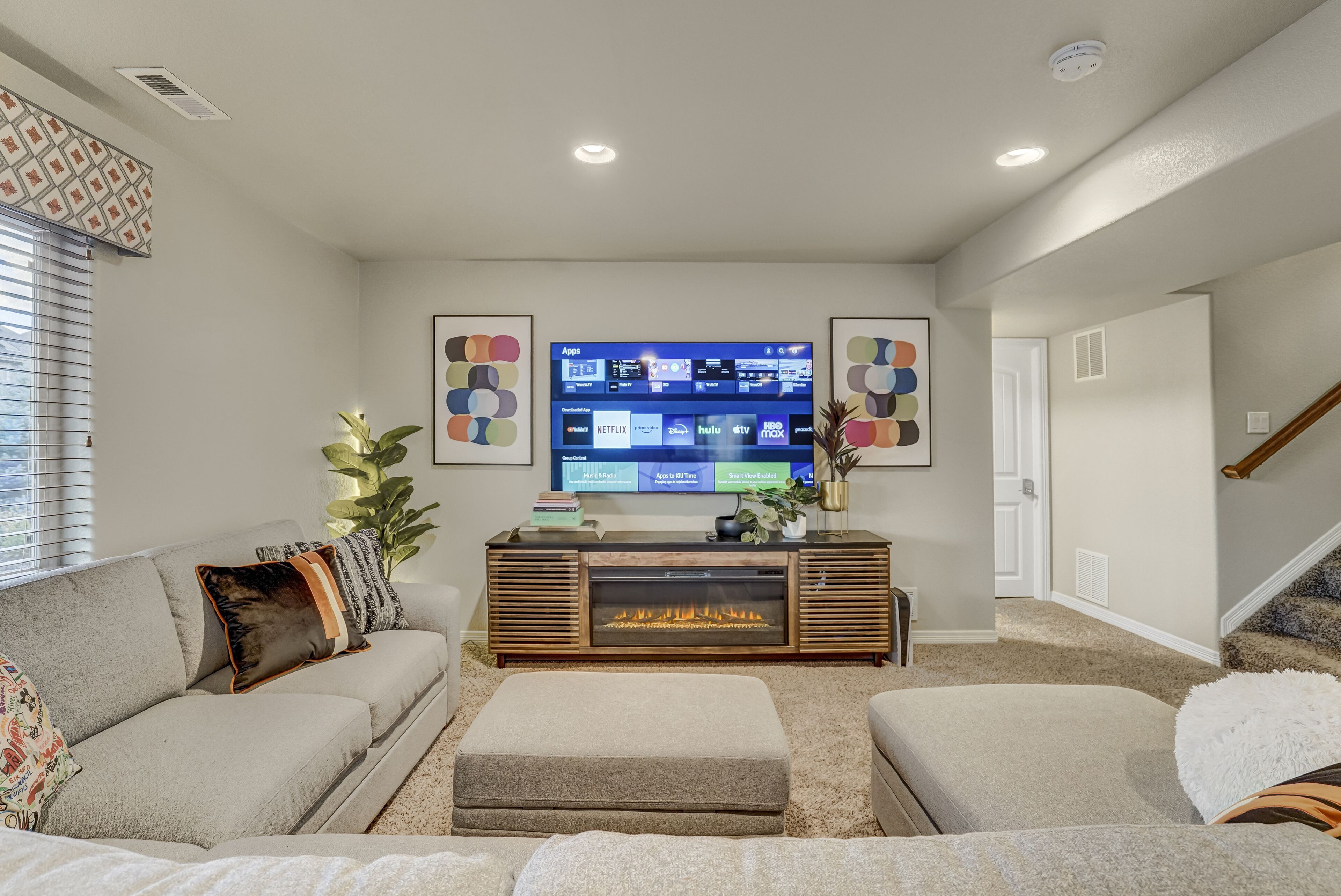 A living room with a large flat-screen TV mounted on a wooden entertainment center, a gray sofa, and a beige carpet.