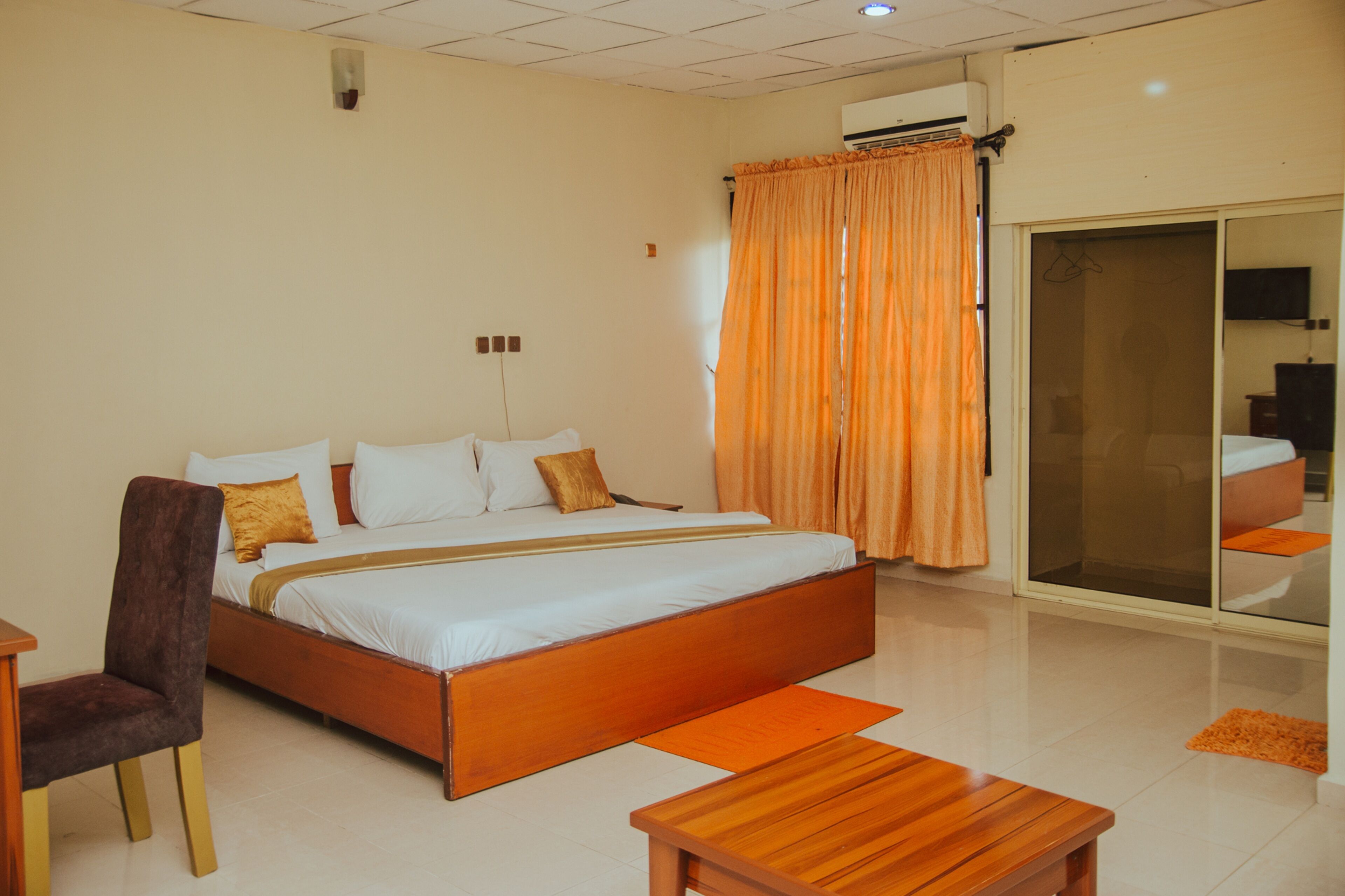 Habitación de hotel con una cama grande, una silla de madera, una mesita y una puerta corrediza de vidrio que da a un balcón.