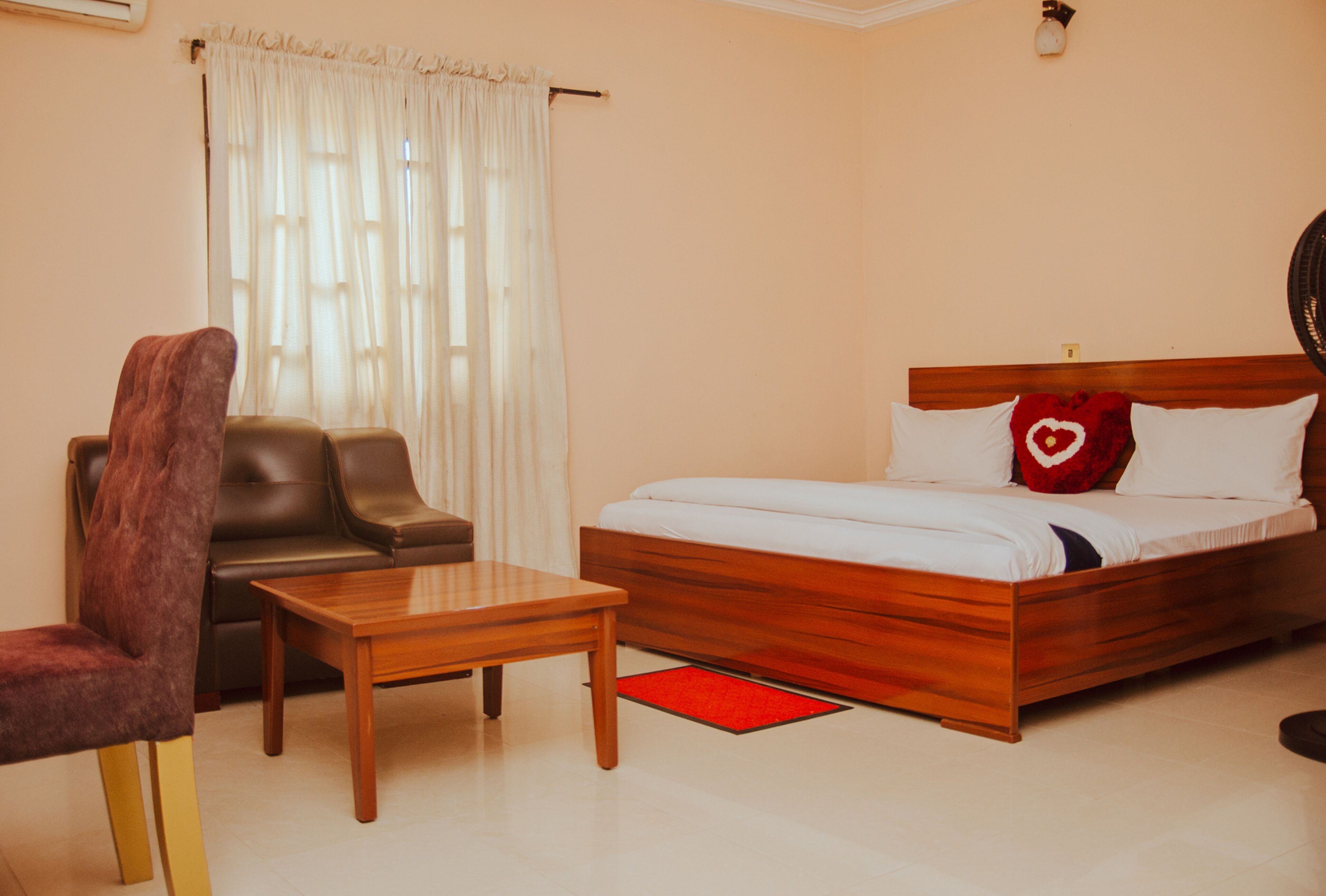 Un dormitorio con una cama de madera, un sofá de cuero marrón, una mesa de centro de madera y una alfombra roja.