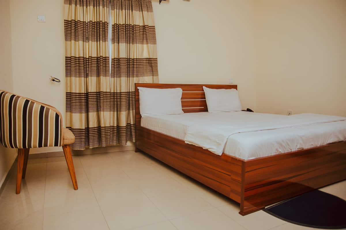 Un dormitorio con una cama de madera, una silla a rayas y una cortina.