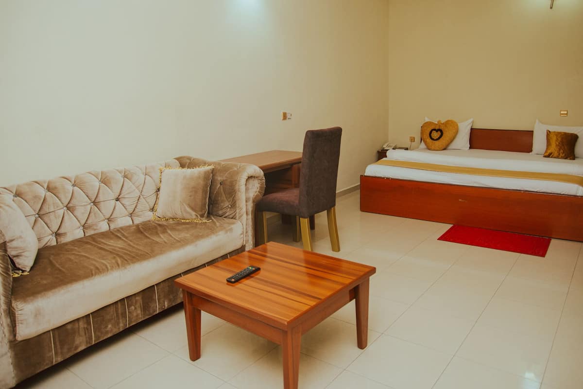Una habitación con un sofá capitonado, una mesa de centro de madera, un escritorio y una cama con un tapete rojo.