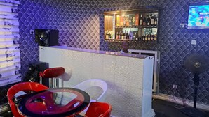 A bar area with a counter, a television screen, and a seating area with a red chair and a glass table. - Haffy Executive Hotels and Suite (Uyo)