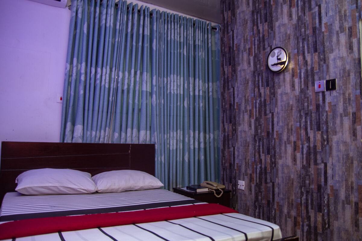 A bedroom with a bed, a telephone, and a wall clock.