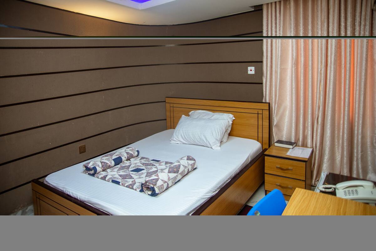 A hotel room with a bed, a bedside table with a phone, and a desk with a chair.