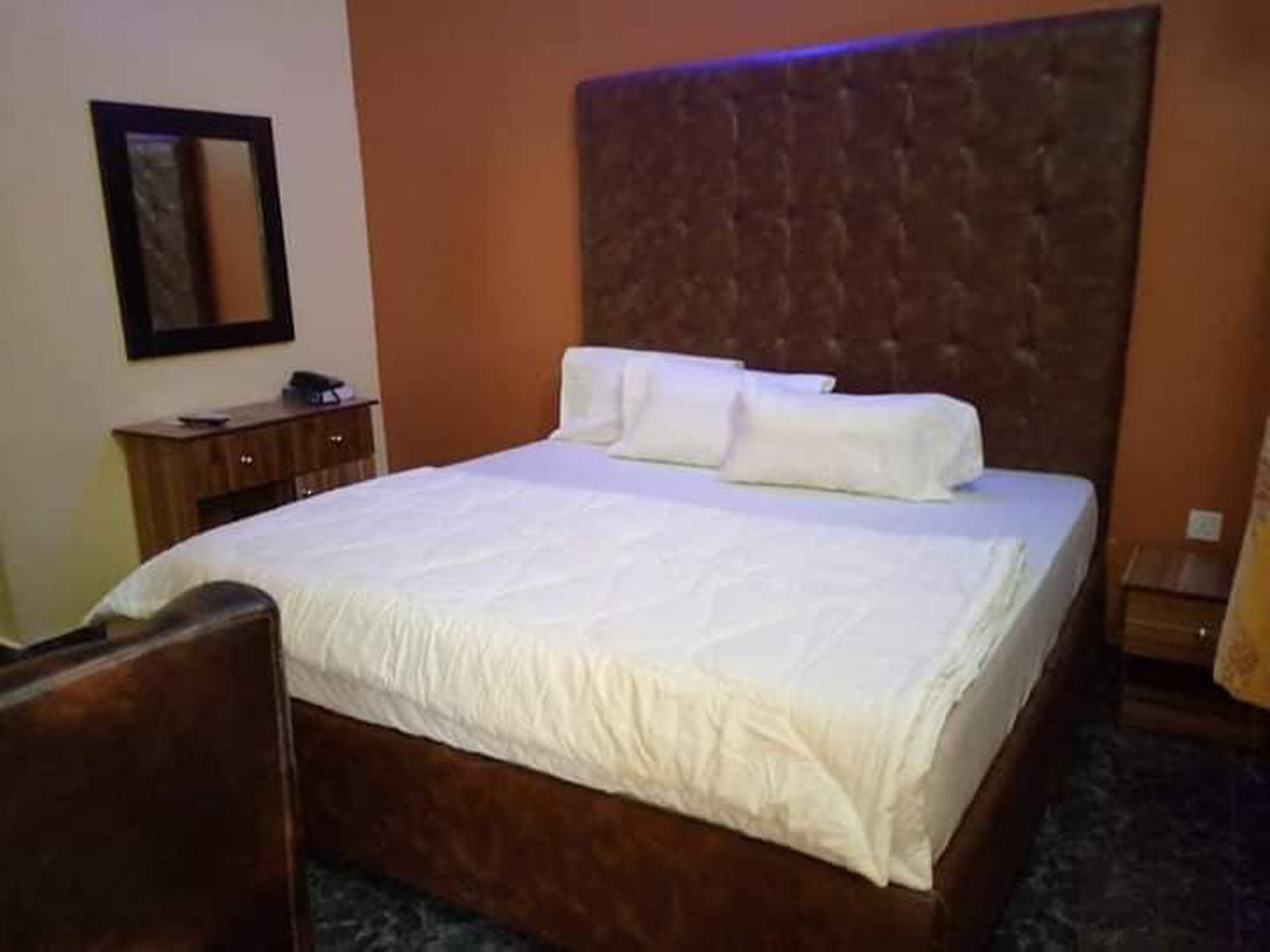 Une chambre d’hôtel avec un grand lit, une tête de lit en bois, une petite commode en bois et un miroir au mur.