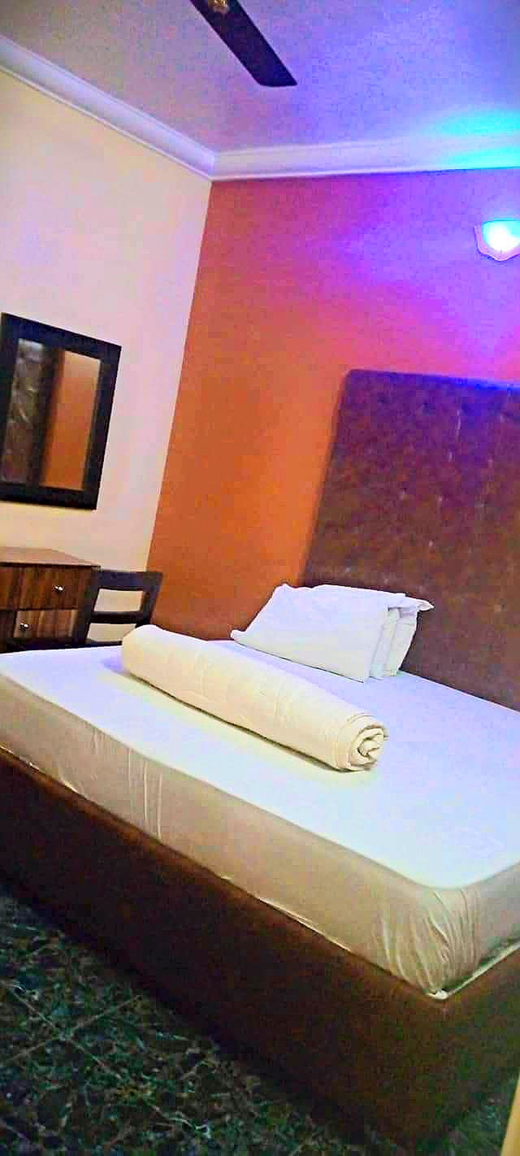 A hotel room with a single bed, a wooden nightstand, a chair, and a mirror on the wall.