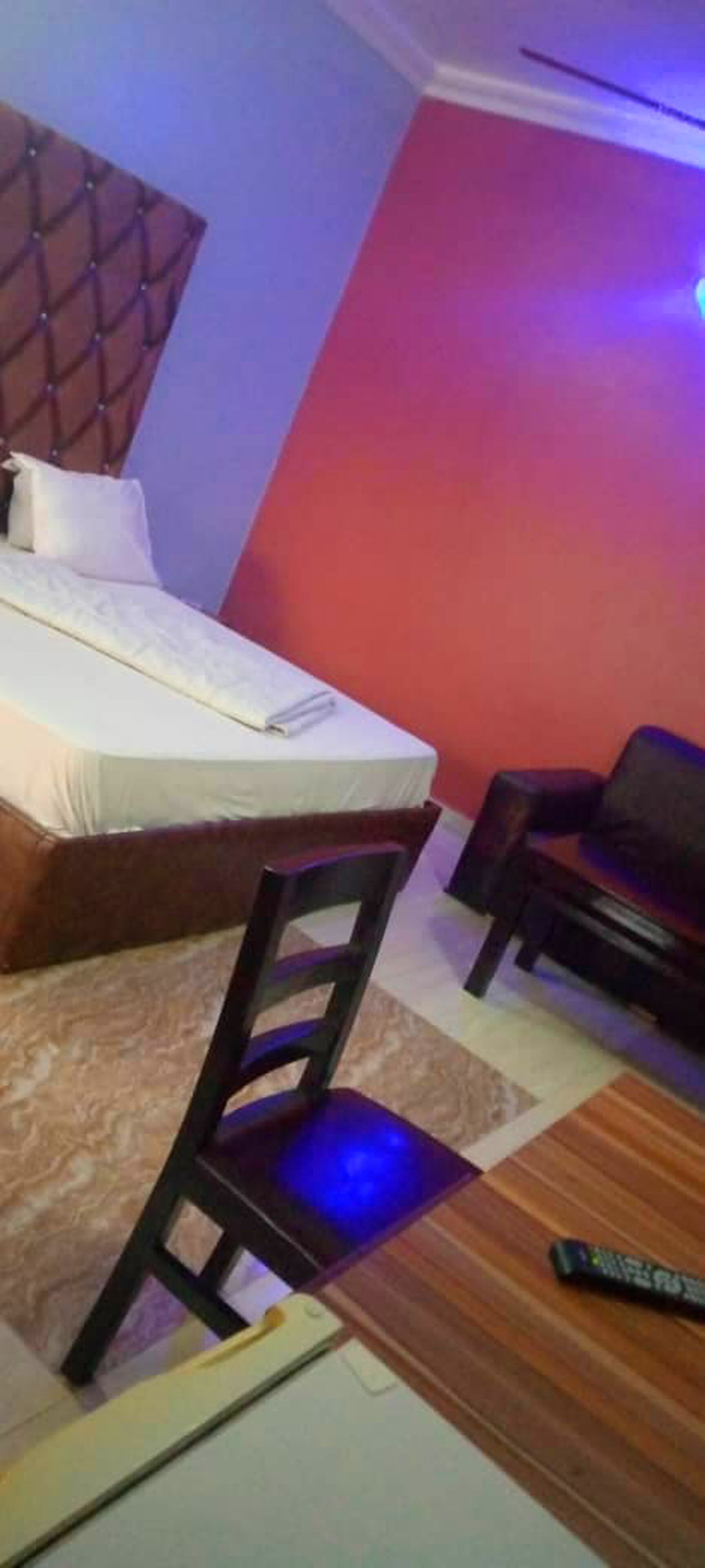 Un dormitorio con una cama, una silla de madera, un sofá y un control remoto en el suelo.
