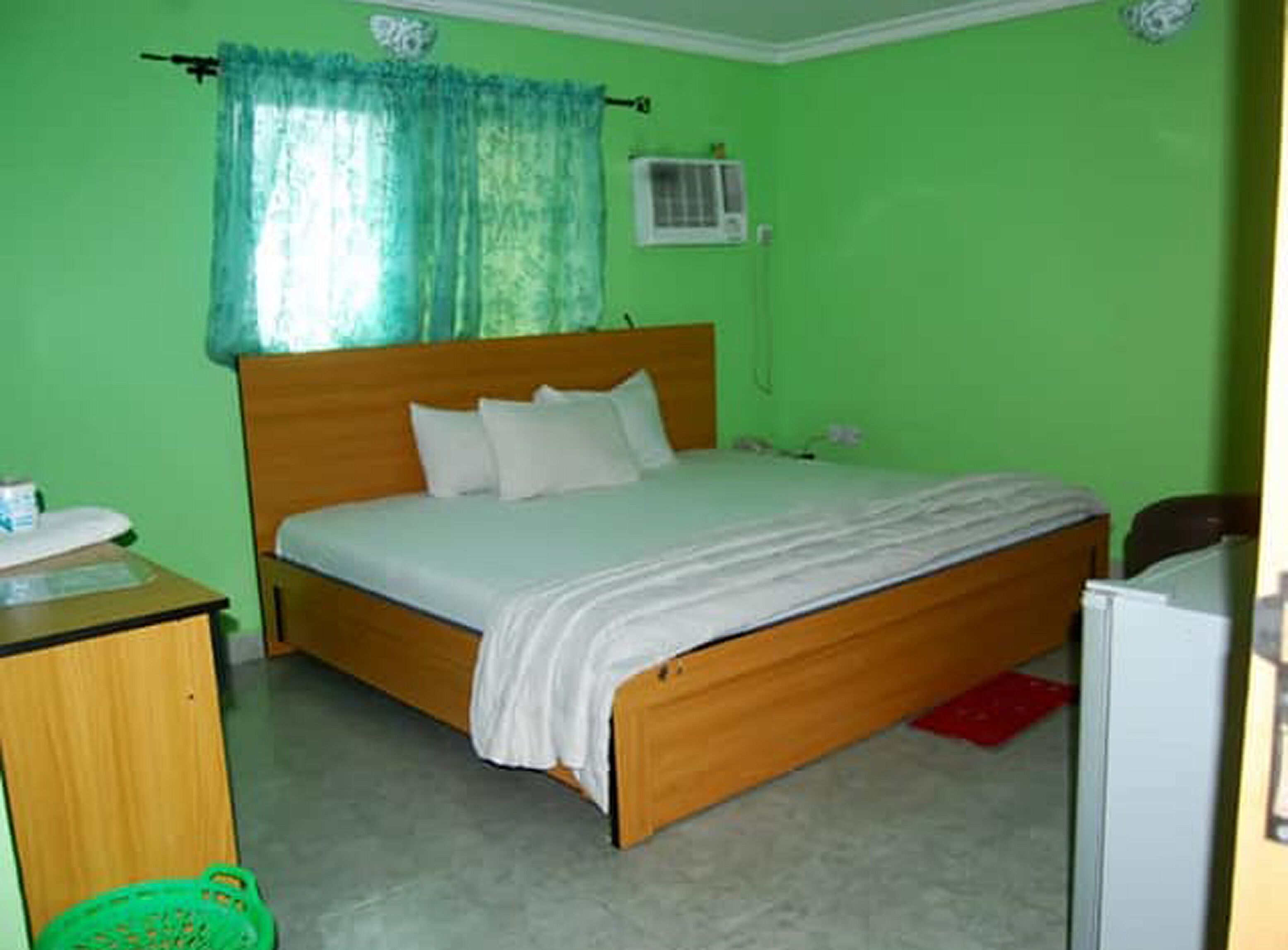 Habitación con una cama individual, cabecera de madera, mesita de noche y pared verde.
