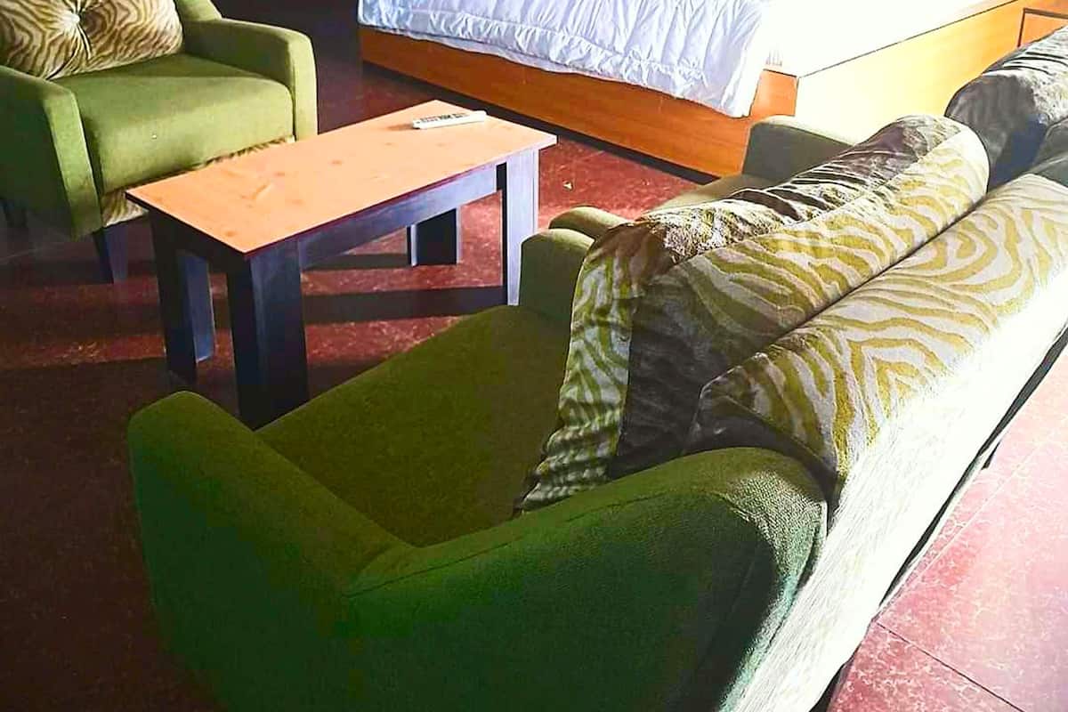 Hotellihuone, jossa on sänky, kaksi vihreää nojatuolia, pieni pöytä ja puinen yöpöytä.