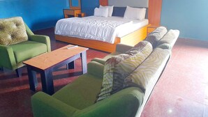 Een kamer met een bed, twee groene banken, een houten tafel en een spiegel.