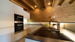 A modern kitchen with a central island, stainless steel appliances, and wooden ceiling beams.