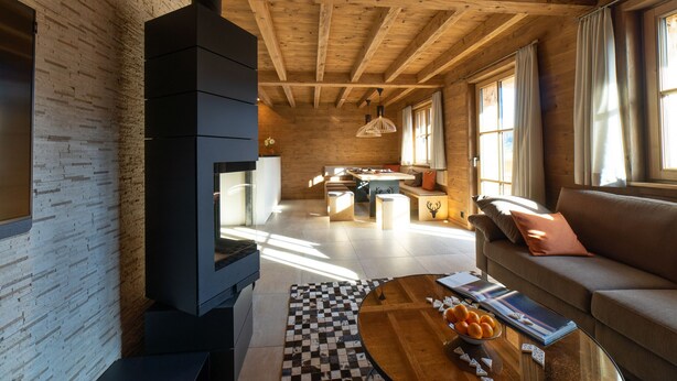 A modern living room with a fireplace, wooden ceiling beams, a sofa, and a dining area.