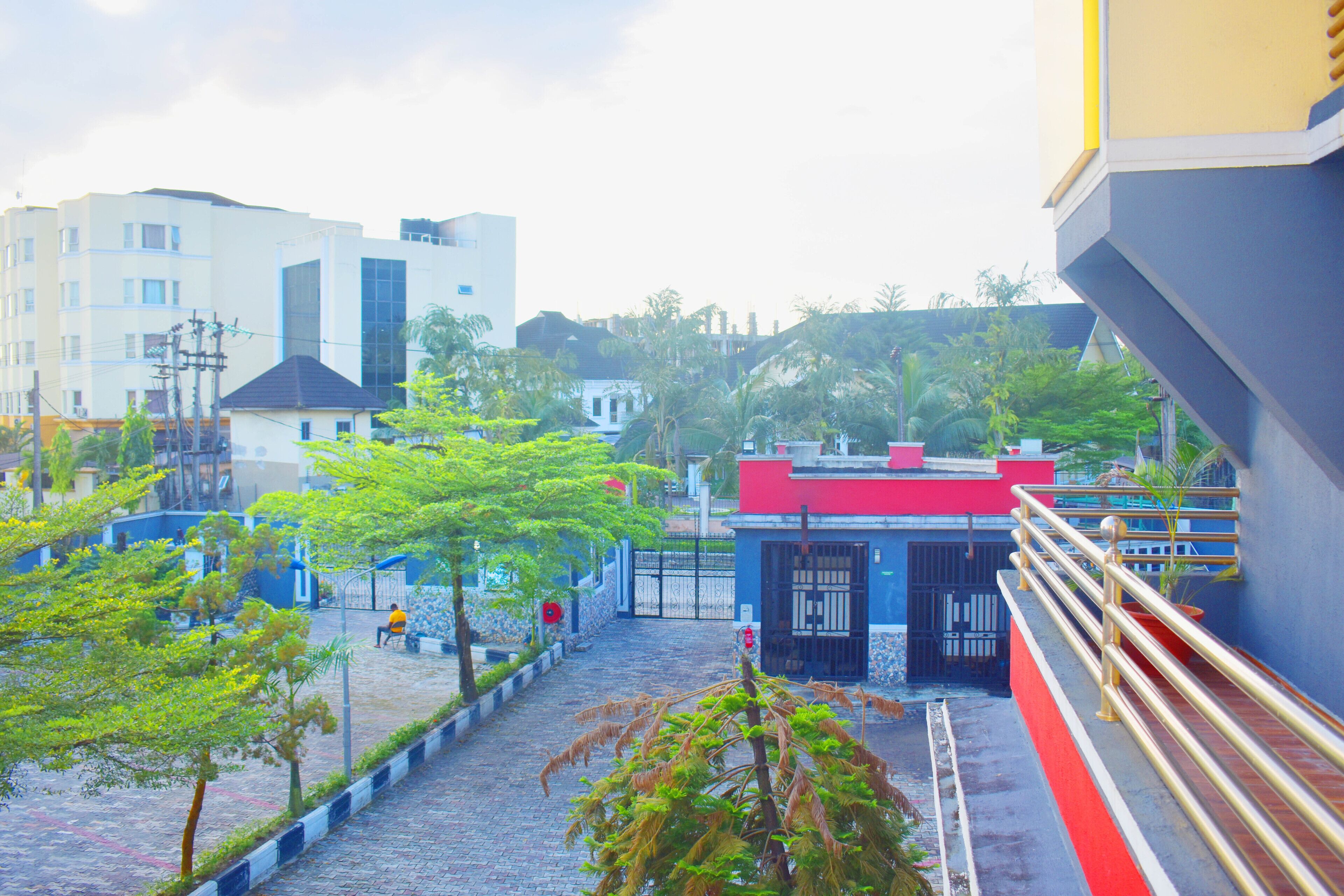 A courtyard with a paved walkway, a red-roofed building, and a white building in the background.