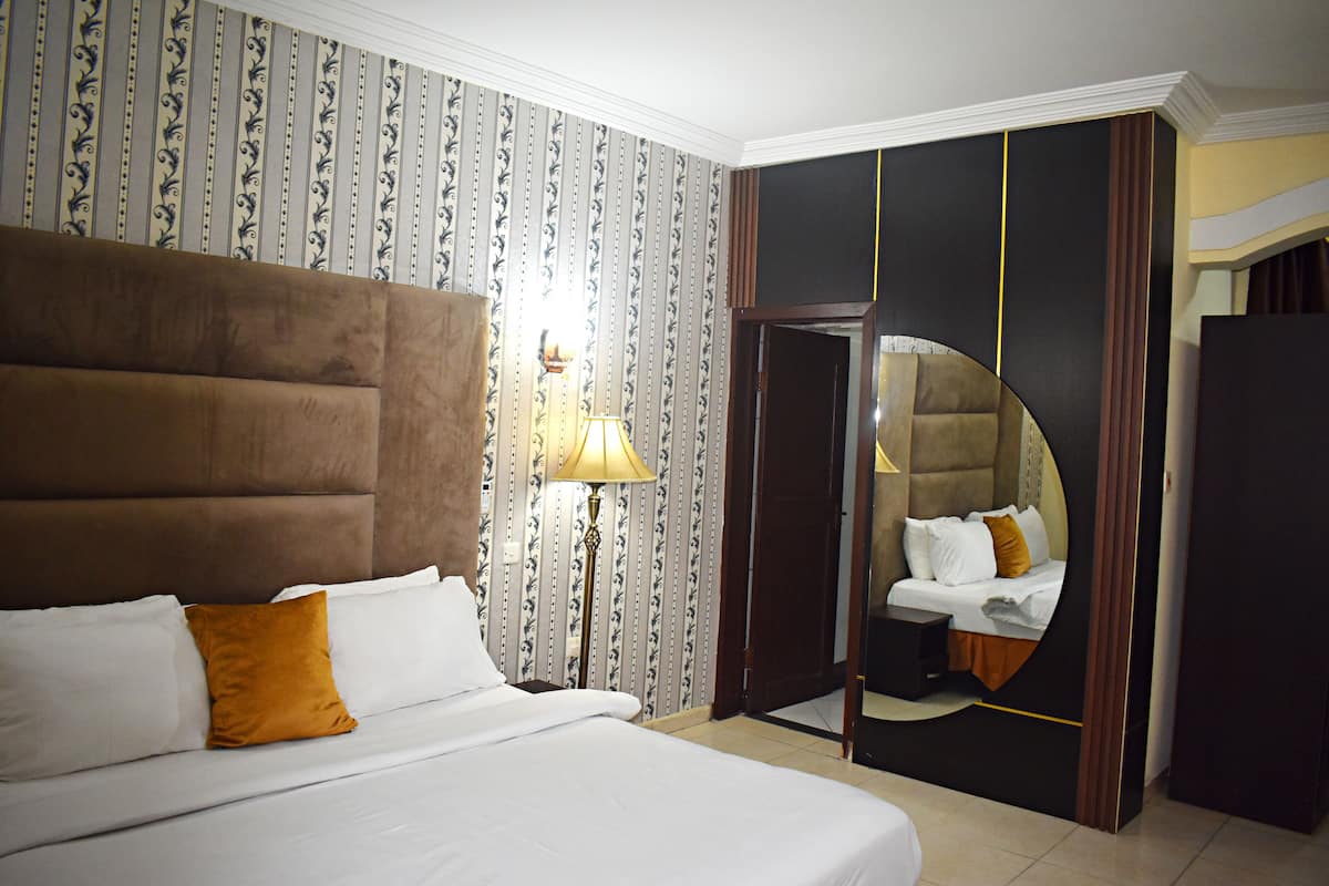A hotel room with a large bed, a nightstand, a lamp, and a mirror.