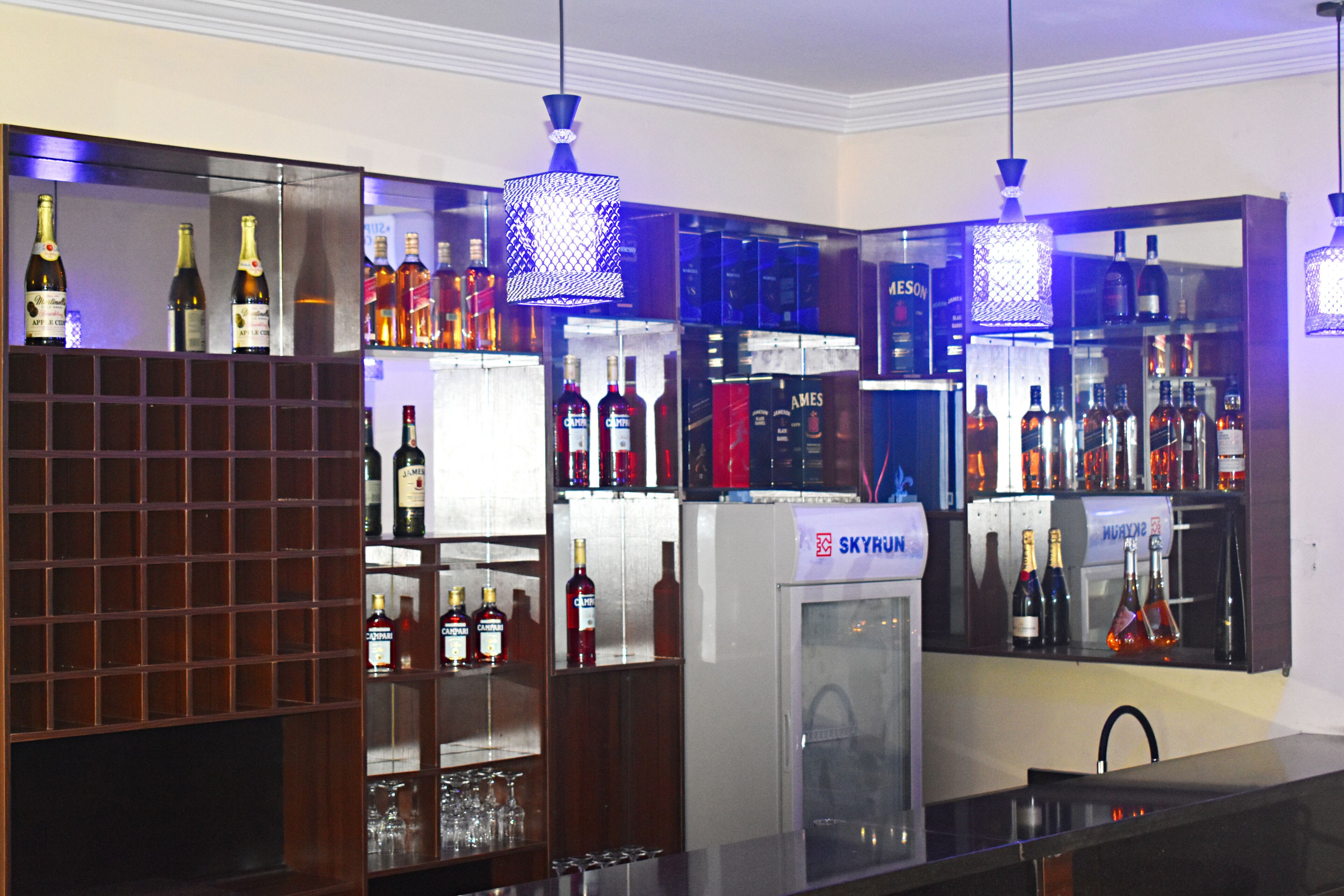 Uma área de bar com prateleiras de garrafas de bebidas, um minibar e luminárias pendentes.