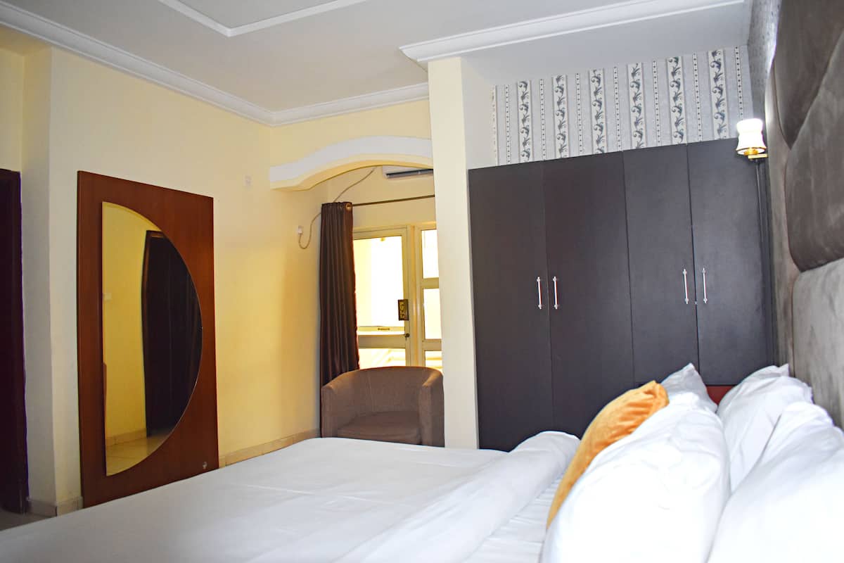 A hotel room with a bed, a wardrobe, a mirror, and a chair.