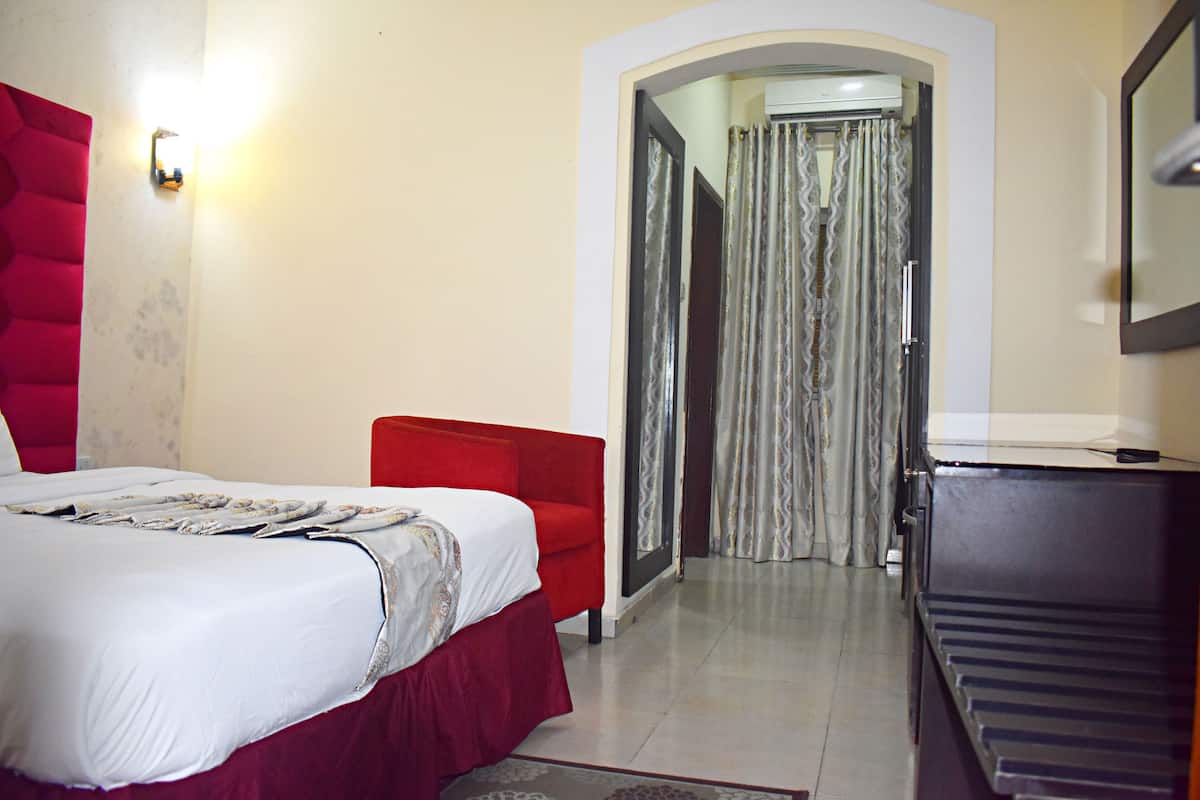 A hotel room with a bed, a red armchair, a piano, and a mirror on the wall.