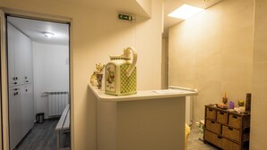 A hotel reception area with a reception desk, a trash bin, a wooden storage unit, and a sign indicating an exit. - Boutique Hotel& Relax Sagittarius (Kyustendil)
