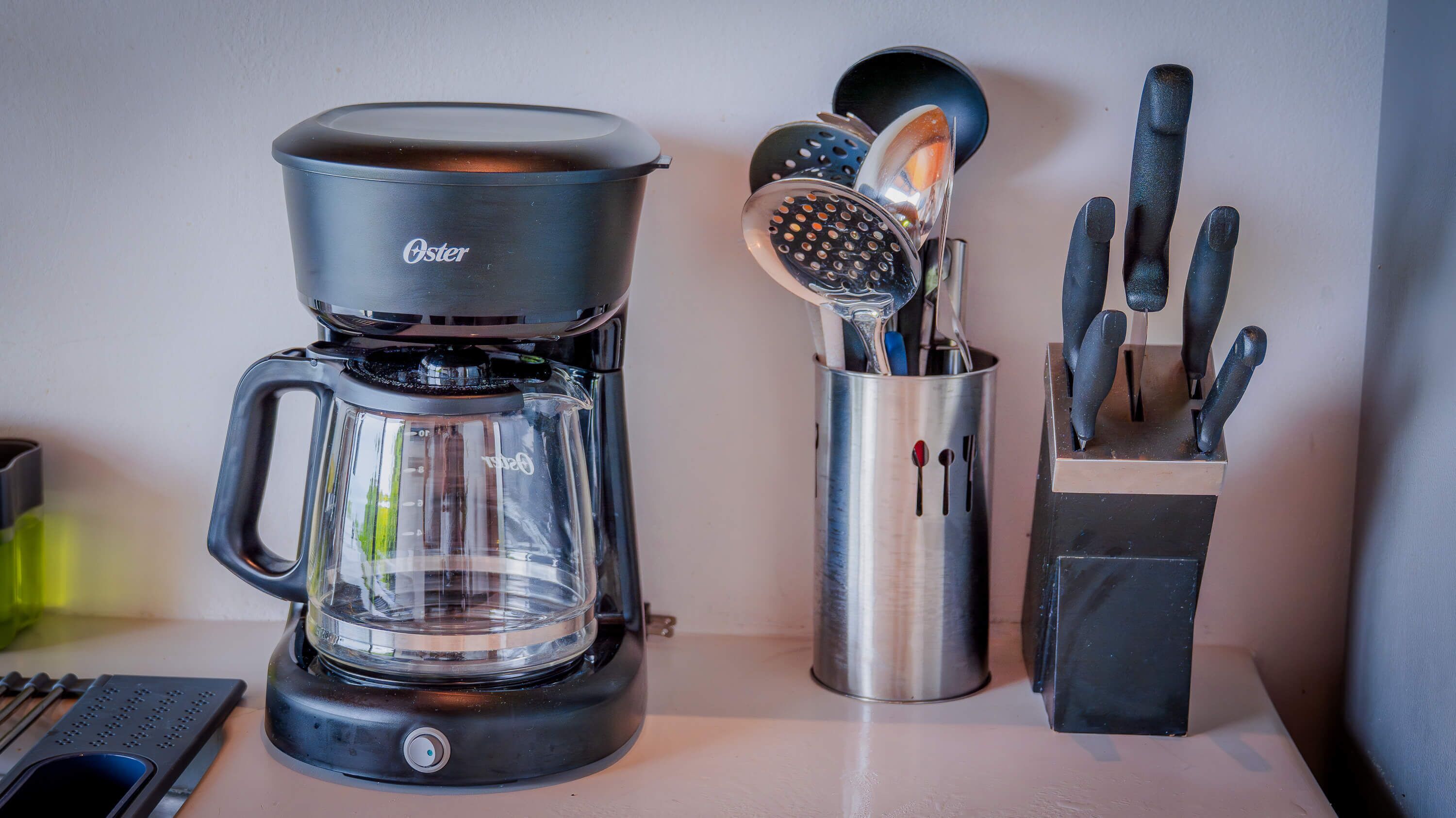 A coffee maker, a colander, and a knife block on a kitchen counter.