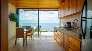 Uma cozinha moderna com armários de madeira, geladeira de aço inoxidável e uma grande janela com vista para o oceano.