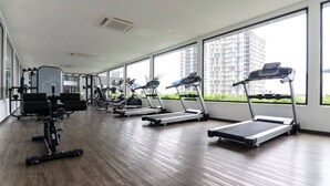 A gym with treadmills, weight machines, and a large window with a view of a high-rise building.