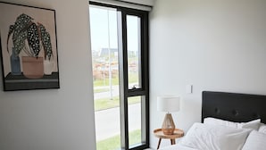 Ein Hotelzimmer mit einem großen Bett, einem Fenster mit Ausblick, einem kleinen Tisch mit Lampe und einem Bild an der Wand.