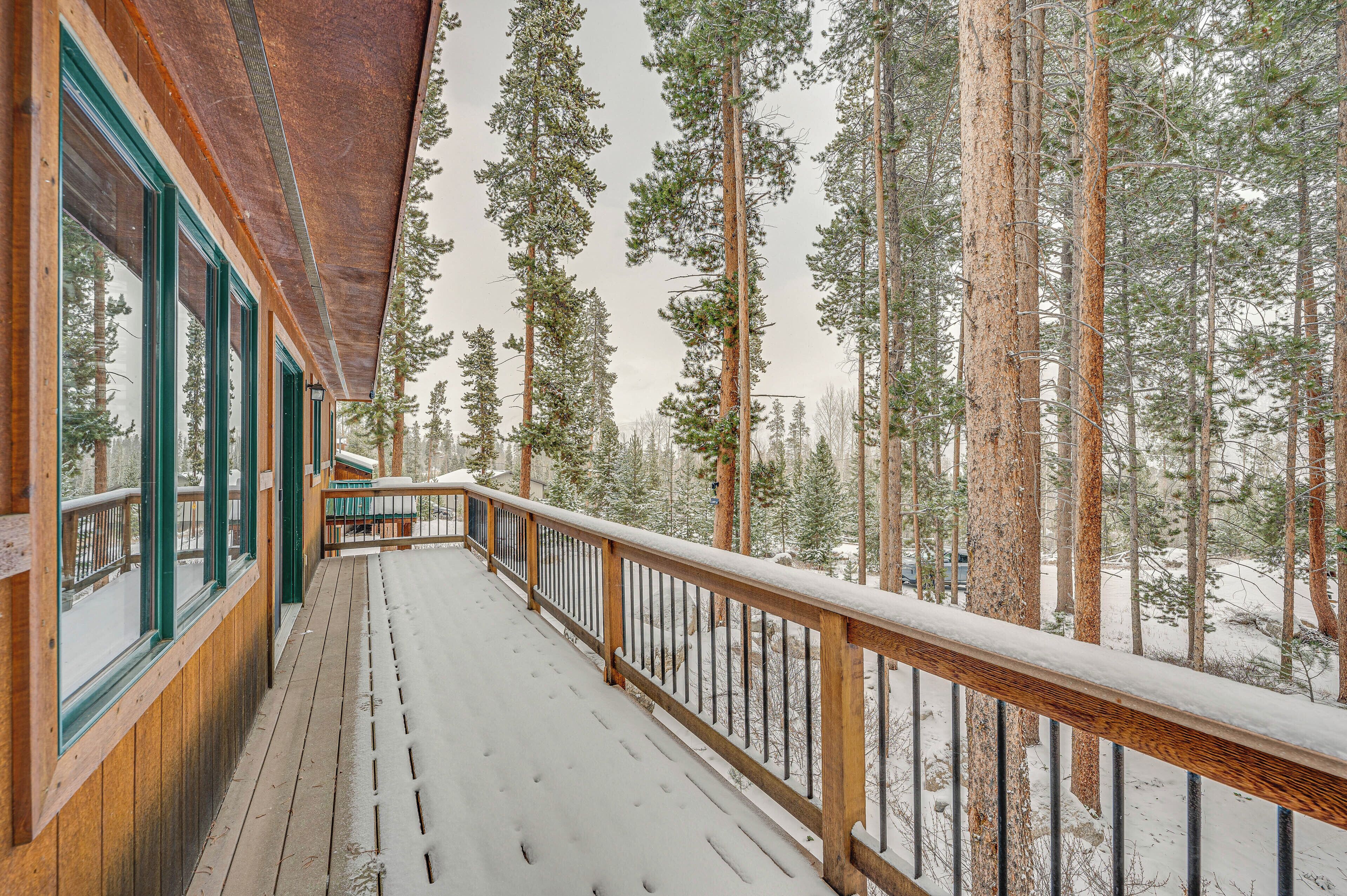 Une terrasse en bois avec une balustrade, de grandes fenêtres et une vue sur de grands pins.