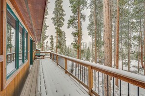 Une terrasse en bois avec une balustrade, de grandes fenêtres et une vue sur de grands pins.