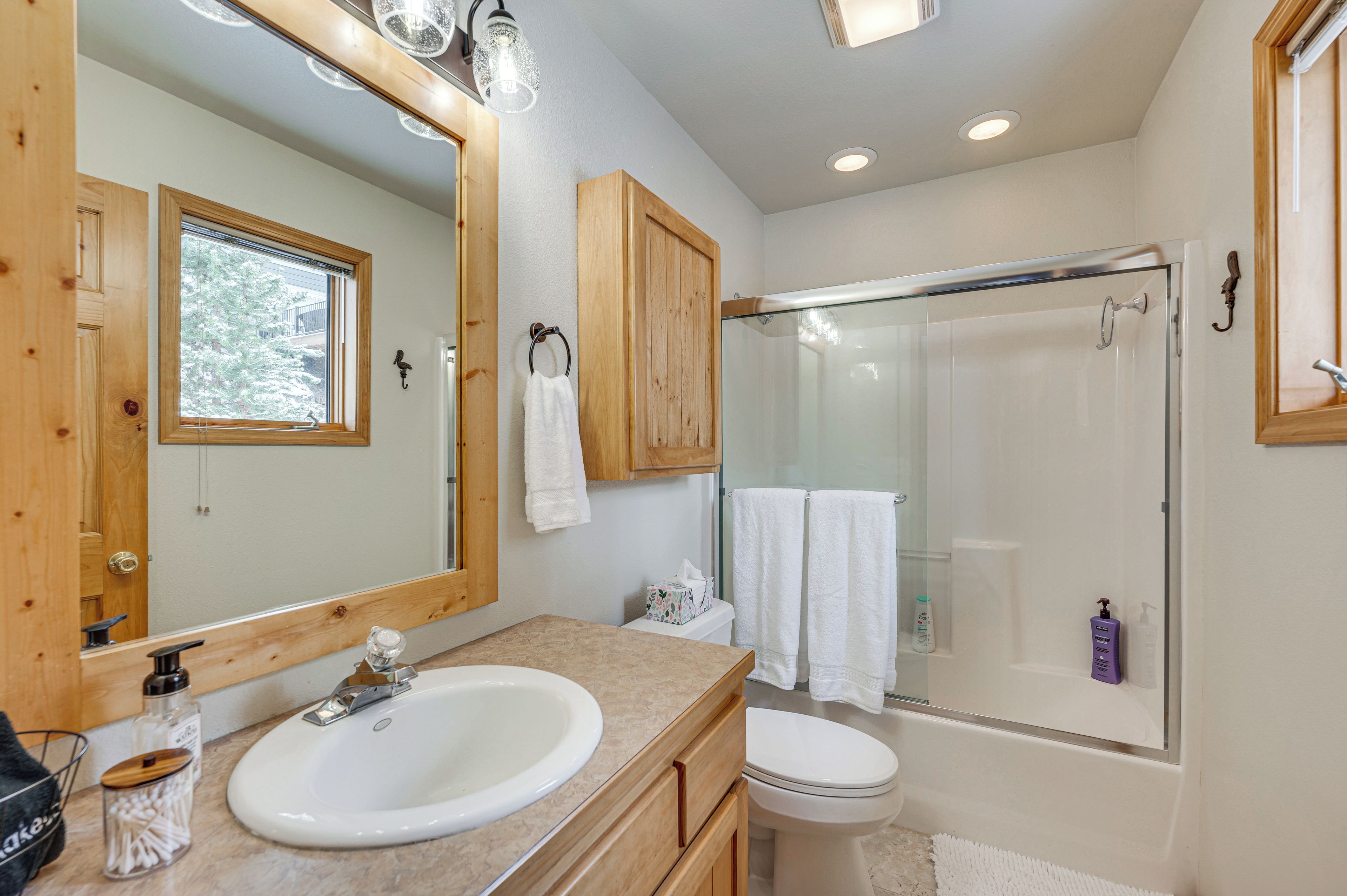 Une salle de bain avec un meuble-lavabo en bois, un grand miroir, une cabine de douche en verre et des toilettes.