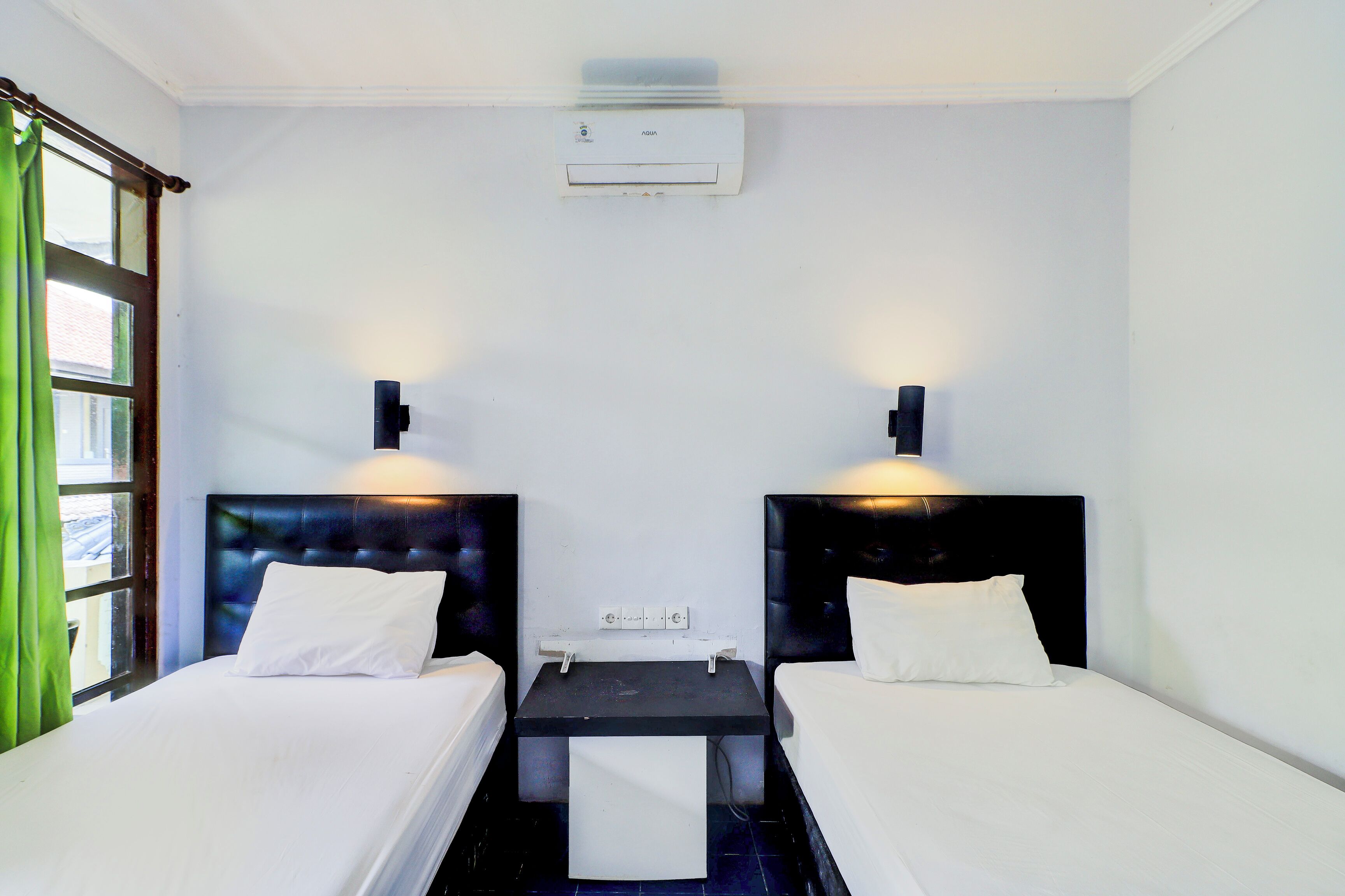 A hotel room with two beds, a small table, and a wall-mounted air conditioner.