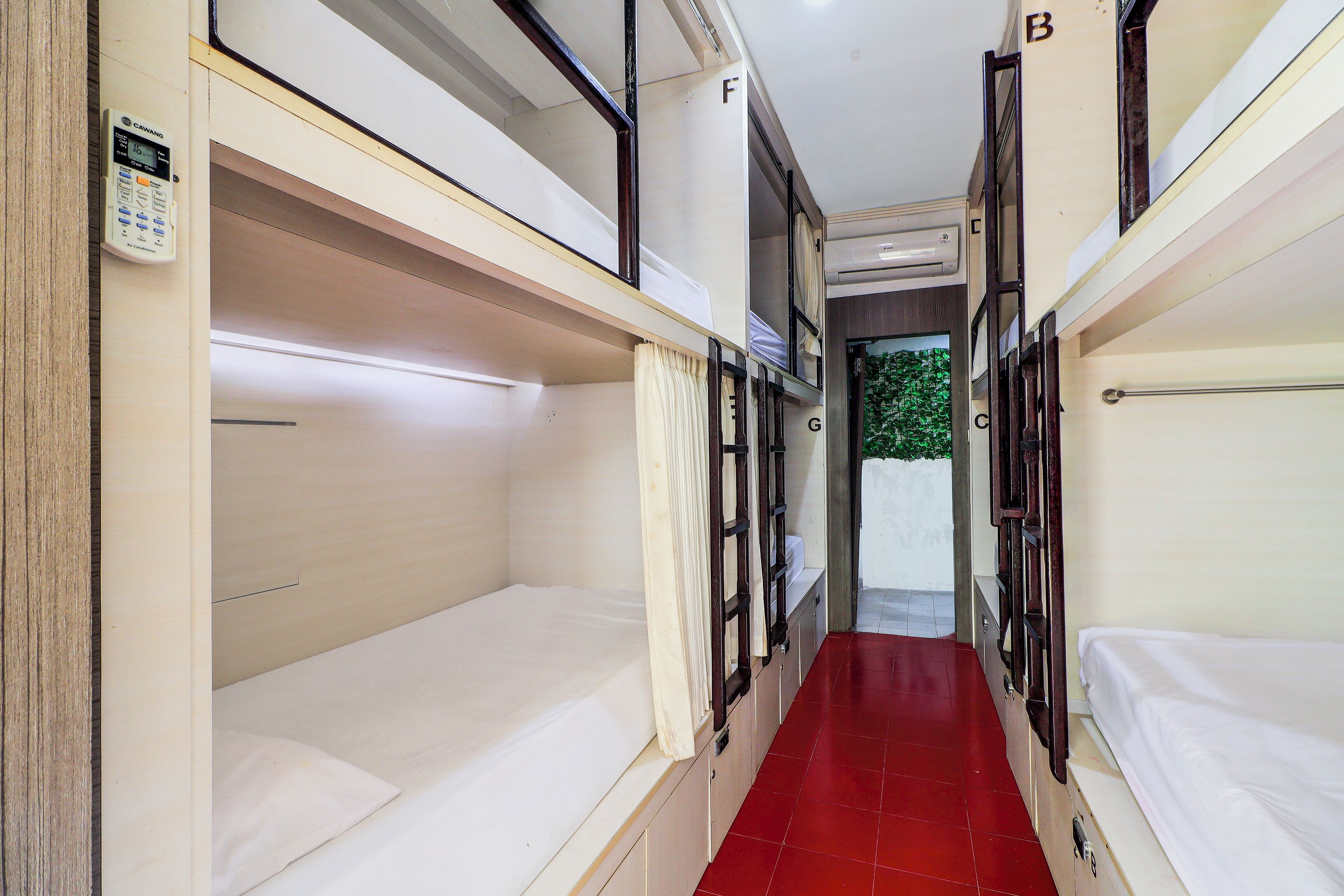 A narrow corridor with bunk beds on either side, a red-tiled floor, and a small air conditioning unit on the wall.