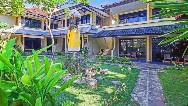 A traditional-style building with multiple floors, large windows, and a well-maintained garden with rocks and plants. - Collection O Legian Near Bimc Hospital Nusa Uda Formerly Anna Kuta Inn (Kuta)