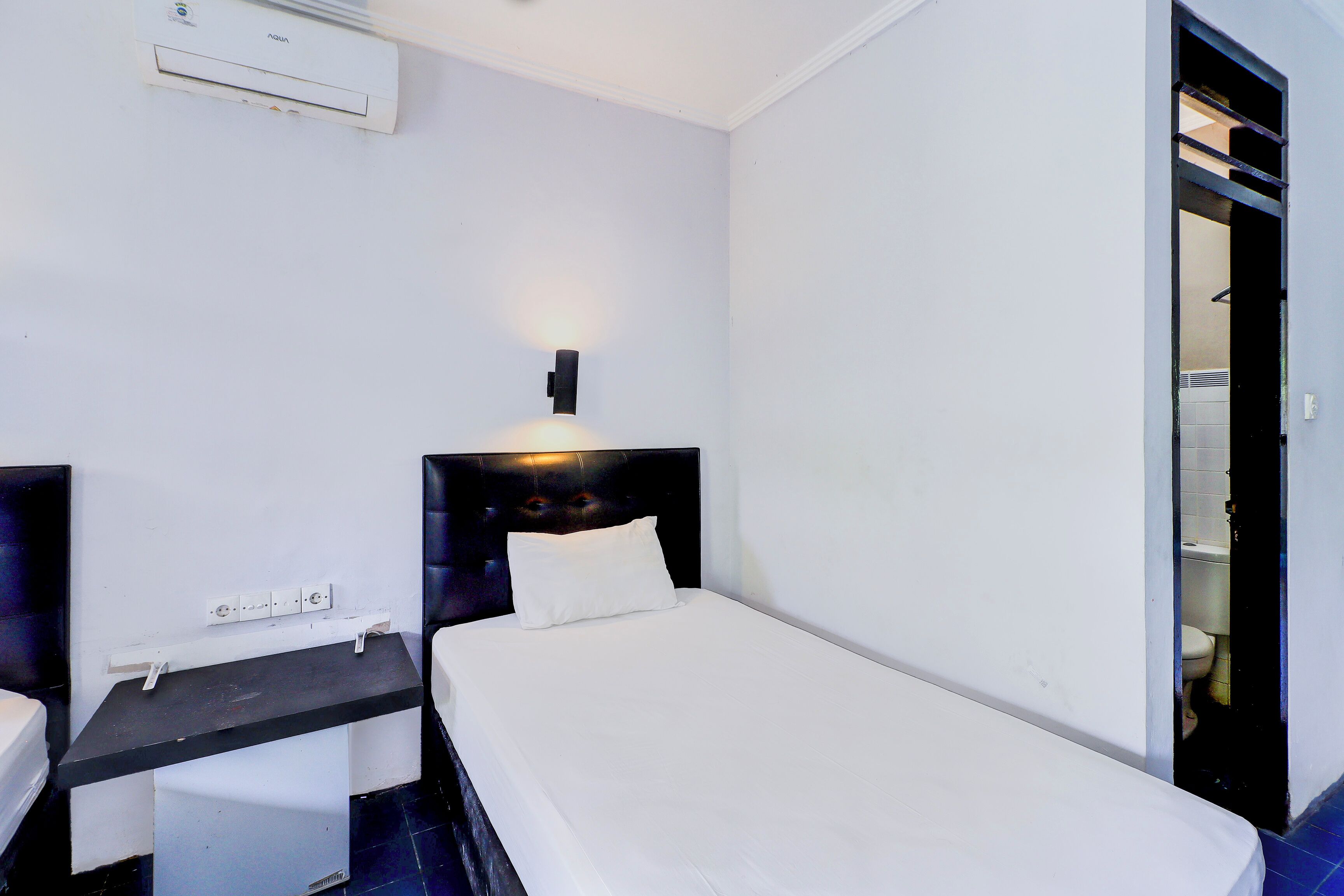 A hotel room with a bed, a desk, and a wall-mounted air conditioner.
