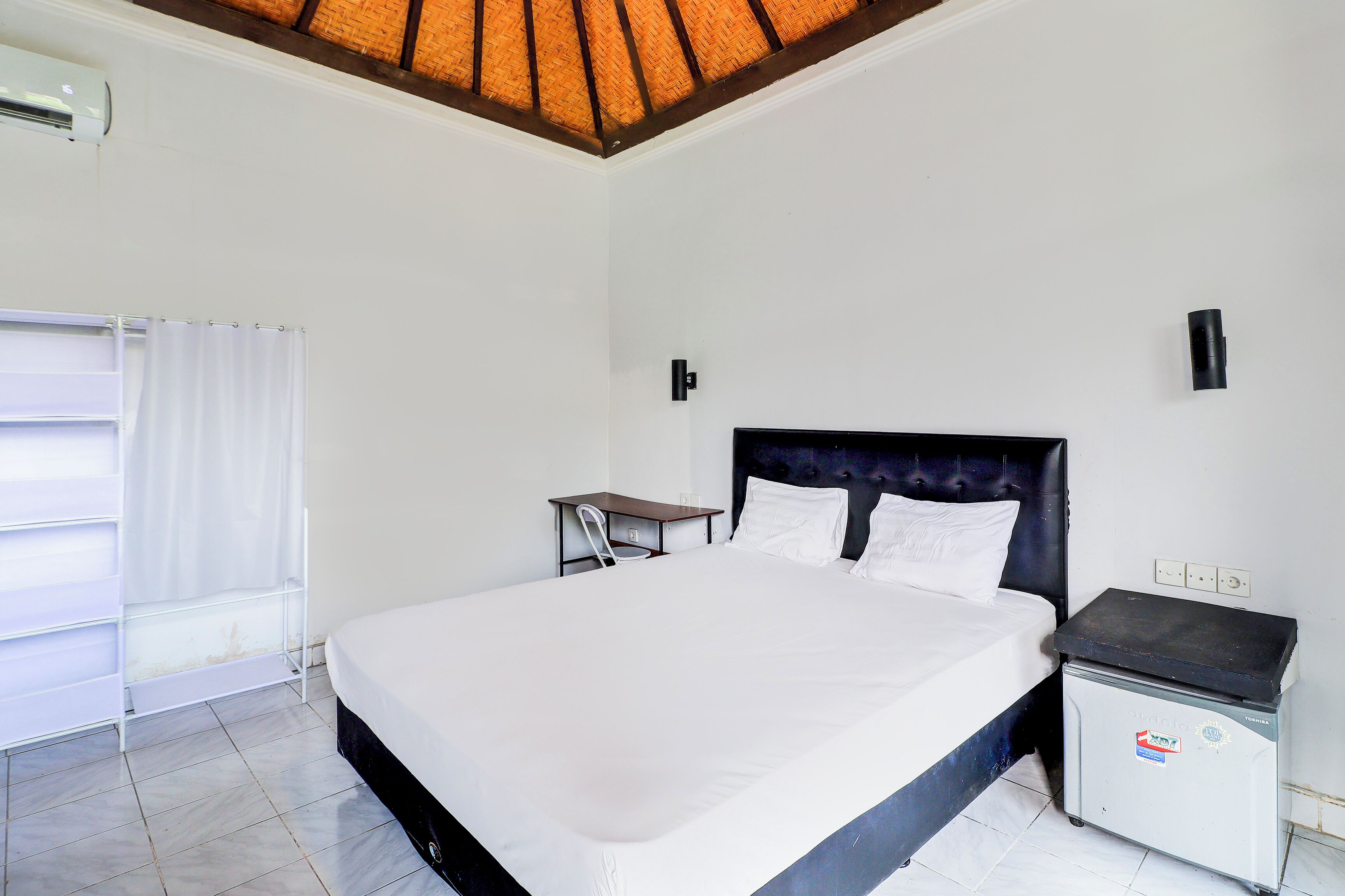 A hotel room with a large bed, a small desk, a nightstand, and a trash bin.