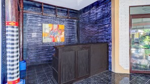 A lobby with a dark wooden reception desk, a blue brick wall, and a glass door leading outside. - Collection O Legian Near Bimc Hospital Nusa Uda Formerly Anna Kuta Inn (Kuta)