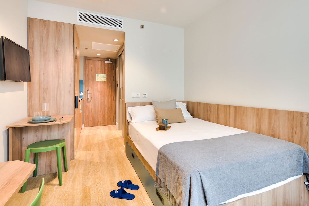 A hotel room with a bed, a desk, a chair, and a TV.