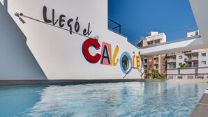 Une piscine avec une grande pancarte sur laquelle on peut lire « Lleó el Calore », et en arrière-plan, une vue sur des immeubles d’habitation.