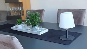 Un comedor moderno con una mesa gris, dos sillas grises, una lámpara blanca y un aparador de vidrio con copas de vino.