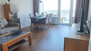 Amplia sala de estar con piso de madera, una mesa de comedor con sillas, un sofá y un televisor sobre un mueble de madera.