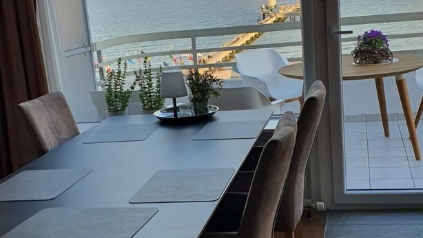 Un comedor con vista al mar, un balcón con plantas y una mesa con sillas.