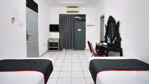 A hotel room with two beds, a desk with a chair, a TV, and an air conditioning unit.