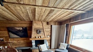 Un salon chaleureux avec des murs en bois, une cheminée, des sièges confortables et une grande fenêtre offrant une belle vue.