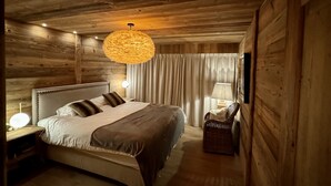 Une pièce chaleureuse aux murs en bois, avec un grand lit, un luminaire suspendu et un fauteuil en osier.