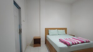 Een slaapkamer met een bed, nachtkastje, een klein houten kastje en een deur.
