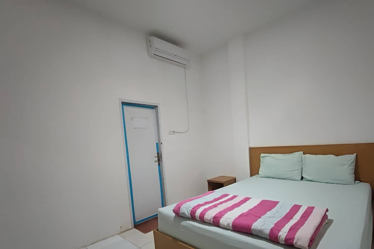 Een slaapkamer met een bed, nachtkastje, deur en airconditioning.