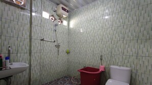 Een badkamer met een betegelde wand, een wit wastafelmeubel, een rode emmer en een wit toilet.